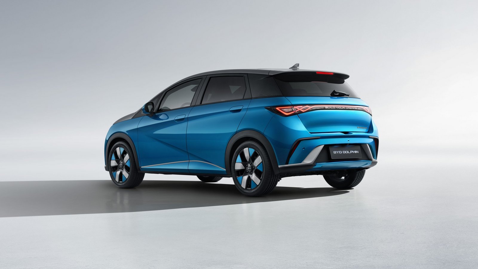 Der BYD Dolphin in Surfing Blue mit Urban Grey Dach steht auf einer offenen Fläche, Sicht schräg von hinten links.